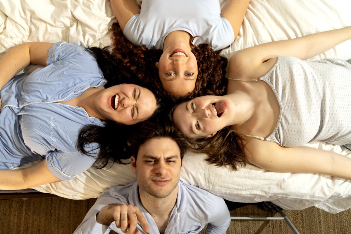 The four members of Skip Skip lying on a bed, heads together in a circle