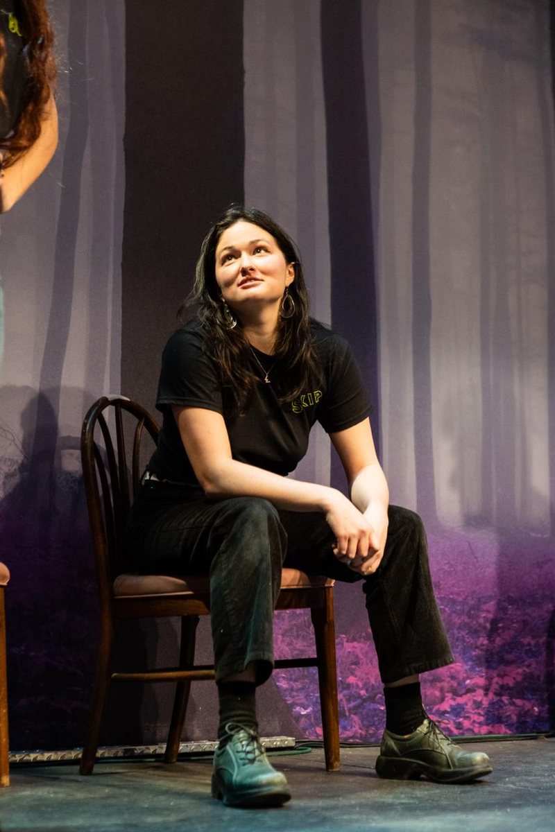 Willa seated on a chair mid-improv-scene in a Skip Skip t-shirt